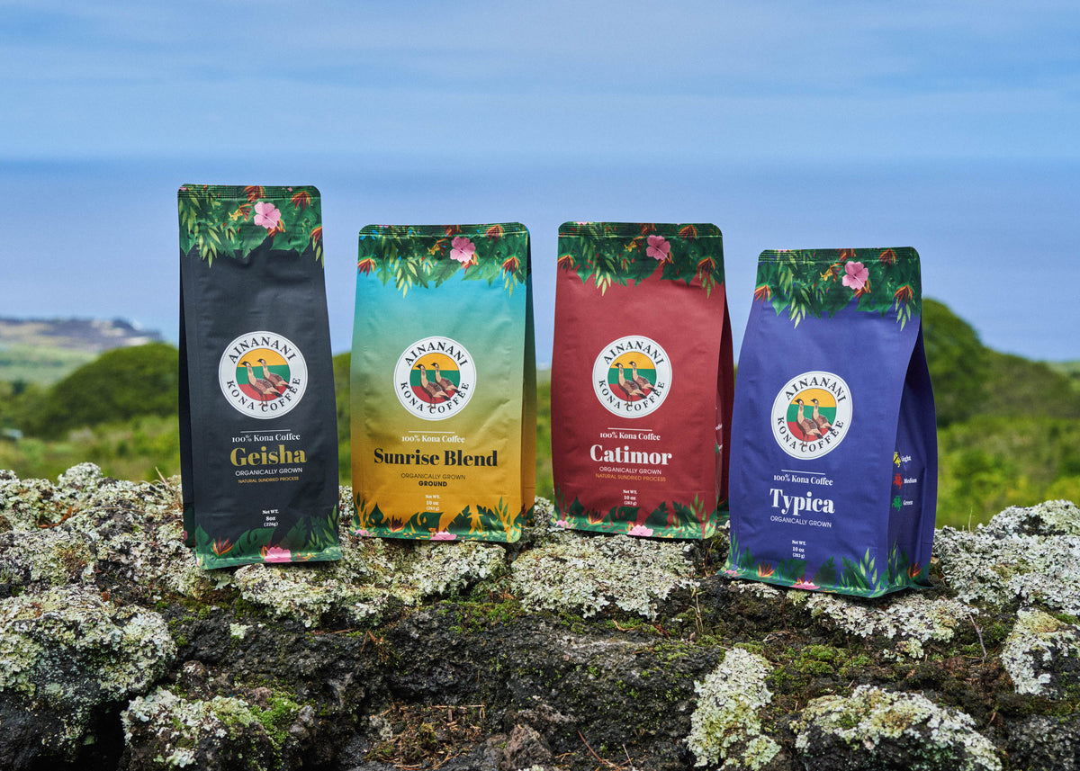Four bags of Ainanani 100% Kona coffee on lava rock by the ocean in Kona, Hawaii