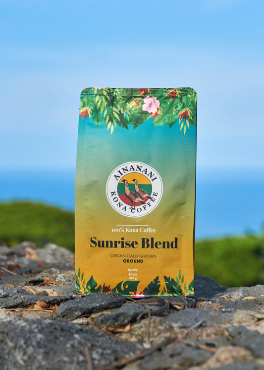Ainanani 100% Kona Sunrise Blend ground coffee bag on lava rock above the ocean